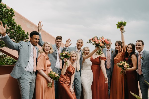 group photo bride bridesmaids groom and groomsmen cheering bouquet in the air