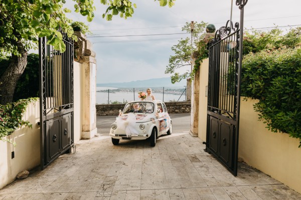 bride is driven through gate entrance she stands and looks out roof