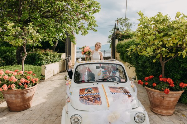 bride is driven through gate entrance she stands and looks out roof