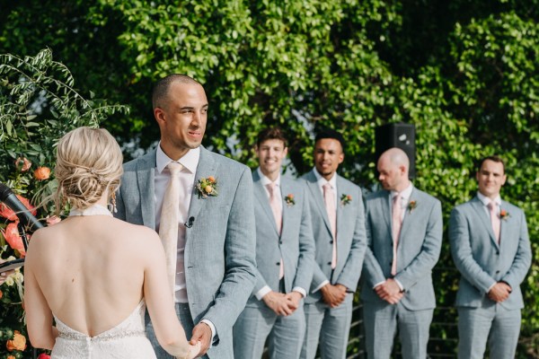 bride and groom hold hands groomsmen in the background