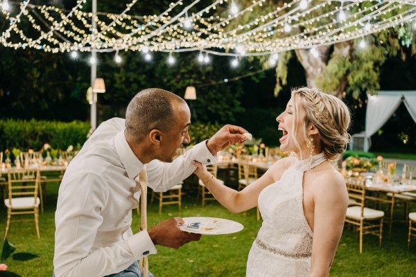 bride and groom laugh as they eat the white wedding cake together