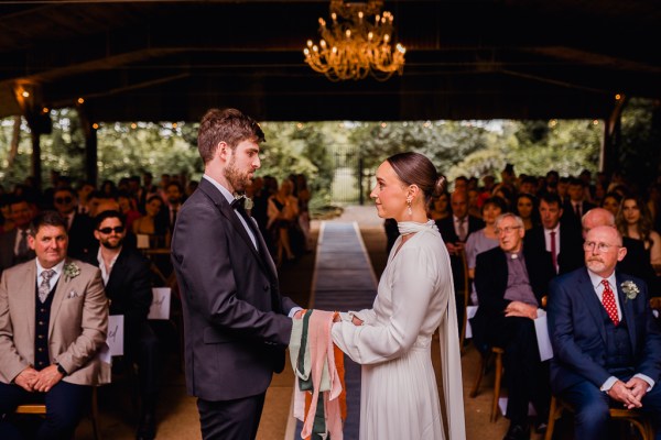 Bride and groom smile in front of guests at alter ribbon bound around wrists