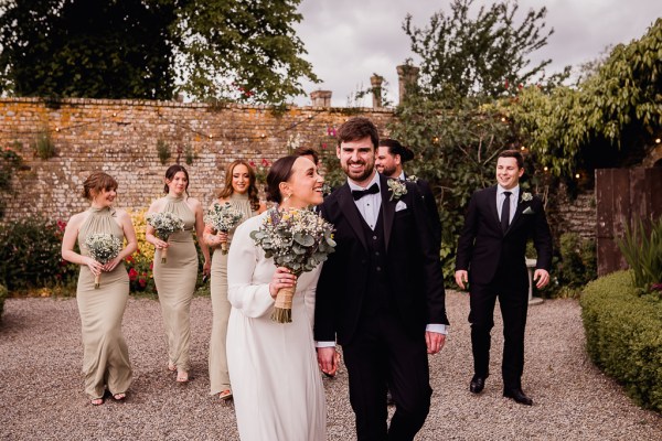 Bride and groom holding hands bridesmaids and groomsmen in the background