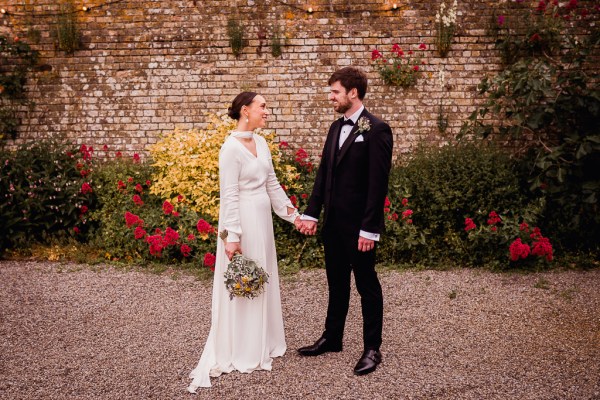 Bride and groom face each other holding hands in the garden together