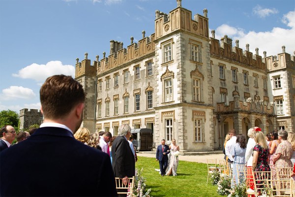 Wide shot of father walking bride daughter down the grassy aisle