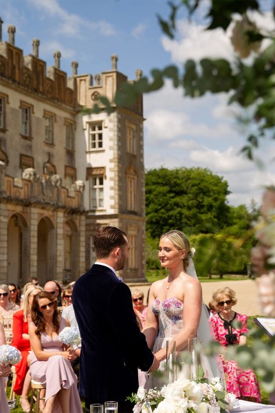 Bride and groom stand in front of guests and castle venue