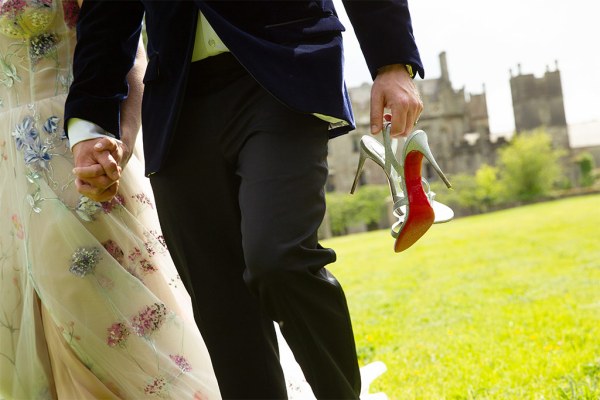 Bride and groom walk groom holds her bridal heels shoes in his hand