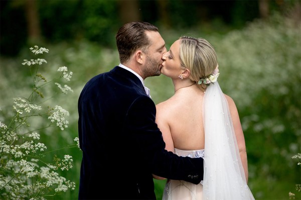 From behind bride and groom veil they kiss are kissing