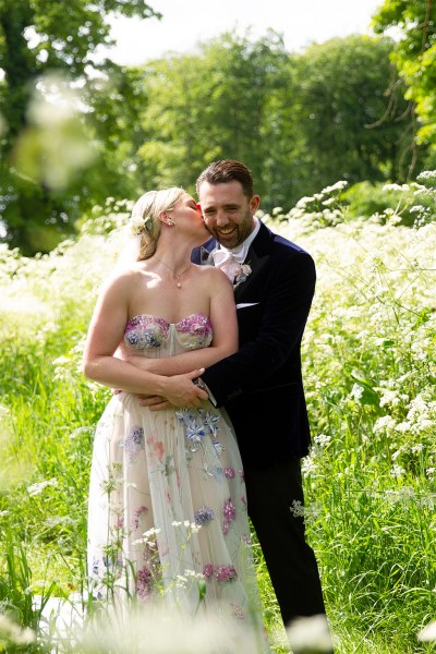 Bride and groom embrace hug in garden park kiss on the cheek