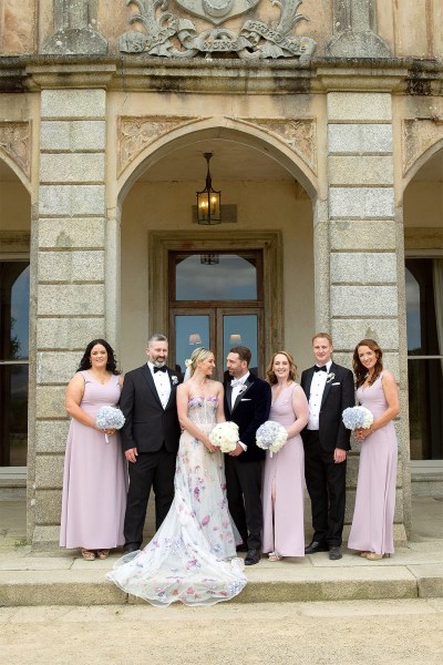 Bride groom bridesmaids and groomsmen stand posing at wedding venue entrance