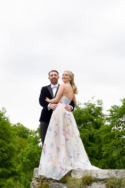 Bride and groom stand on ledge balcony to wedding venue holding each other and smiling