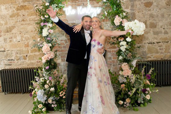 Bride groom stand in front of flower decoration hands in the air