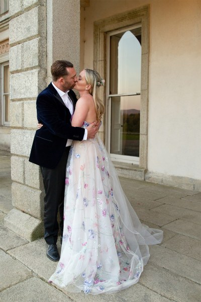 Bride and groom exterior shot evening shot outside wedding venue they hug kissing