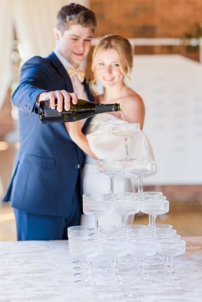 Bride and groom pour bottle of champagne over fountain glasses