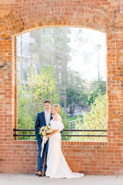 Bride and groom stand in front of bricked wall