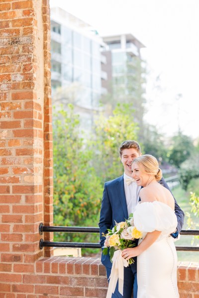 Bride and groom stand in front of bricked wall