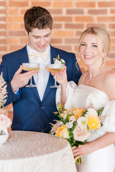 Bride and groom smile as they cheers with glasses of champagne