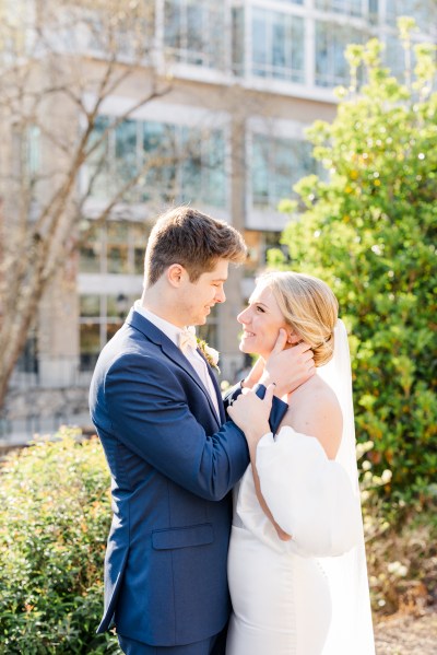 Groom touches brides cheek as they look at each other in garden setting