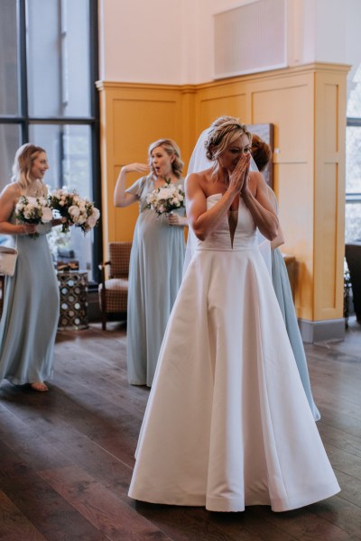 Bride cups hands over face bridesmaids in background holding bouquets