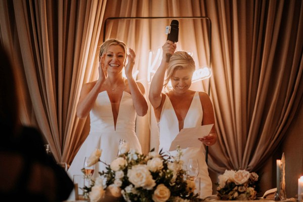 Brides clap and celebrate at dining room table covered in flowers