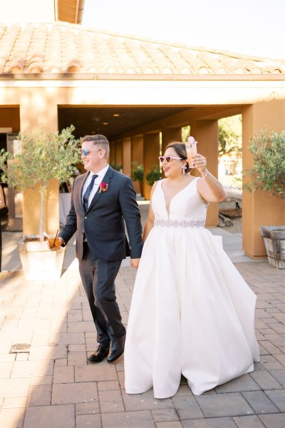 Bride and groom wearing sunglasses waving to crowd/guests