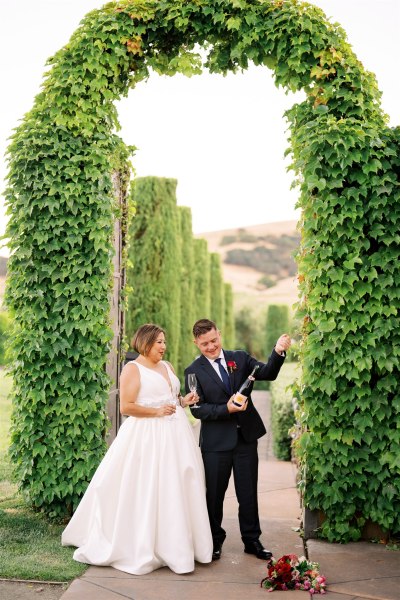 Bride and groom standing in garden opening champagne