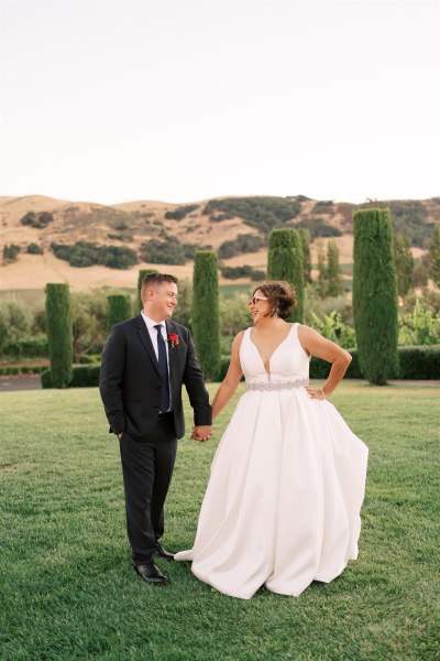 Bride and groom standing on the grass holding hands