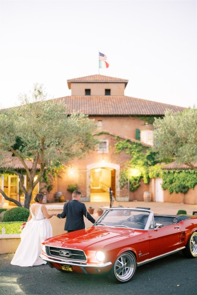 Red car couple in front of wedding venue they walk towards entrance