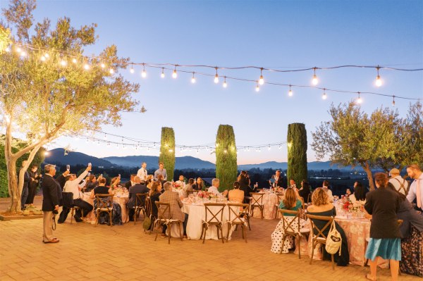 Wide shot evening time view of guests seated exterior tables fairy lights