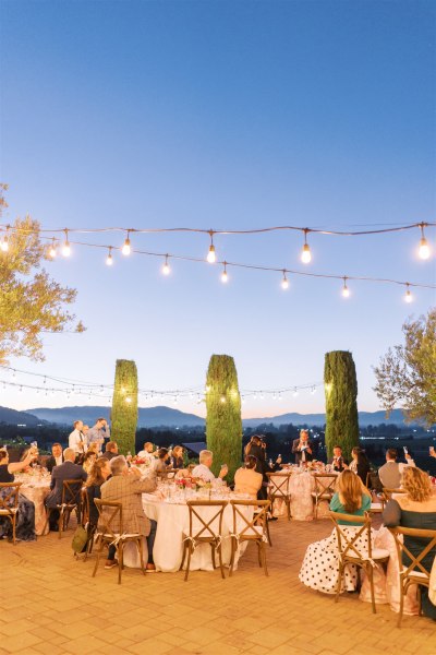 Wide shot evening time view of guests seated exterior tables fairy lights