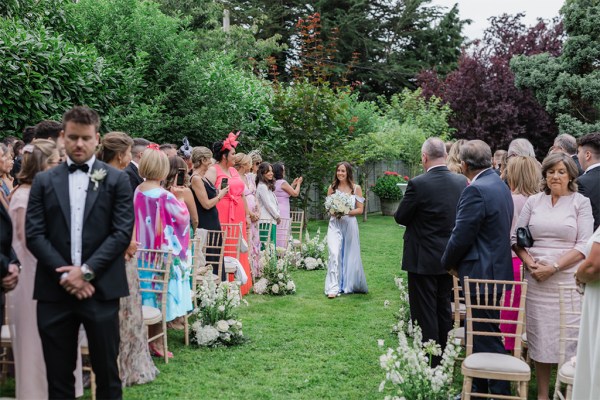 one of the bridesmaids walks down the aisle walking on the green grass