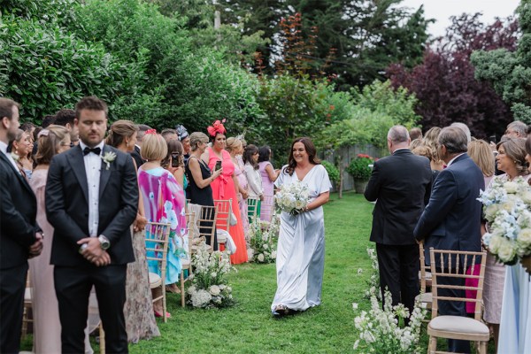 one of the bridesmaids walks down the aisle walking on the green grass