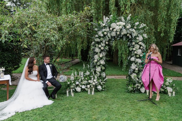 bride groom and celebrant/woman in pink reads speech at alter setting