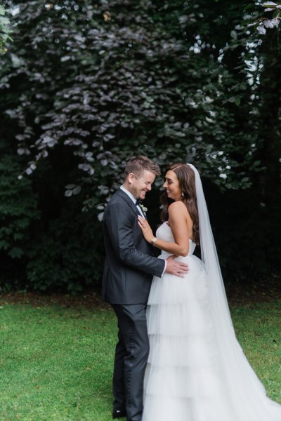 bride and groom pose in the garden together on the green grass