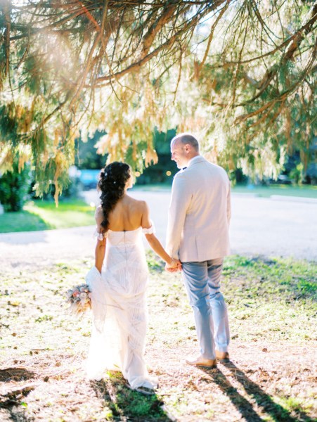 Bride and groom standing in forest setting sun is shining they hold hands