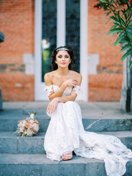 Bride sits on venue steps bouquet sits beside her