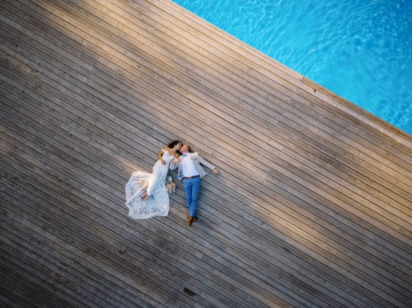 Blue pool view and bride and groom lying flat drone shot footage