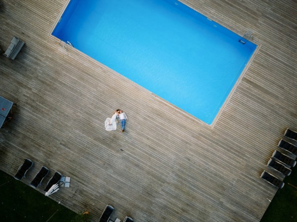 Blue pool view and bride and groom lying flat drone shot footage