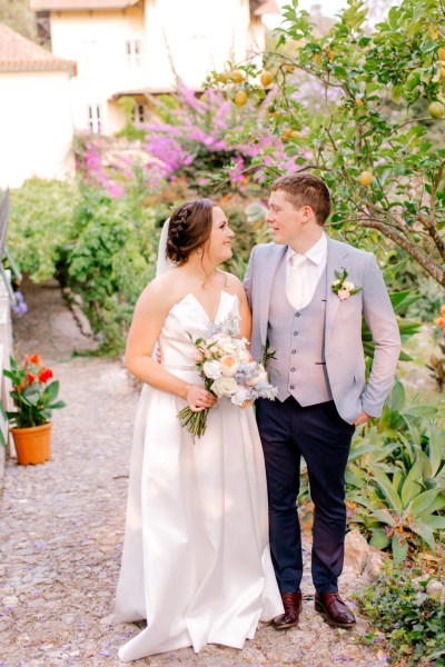 bride and groom in garden she holds bouquet they look at each other