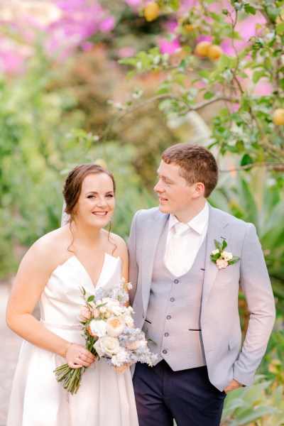 bride and groom in garden she holds bouquet he looks at her