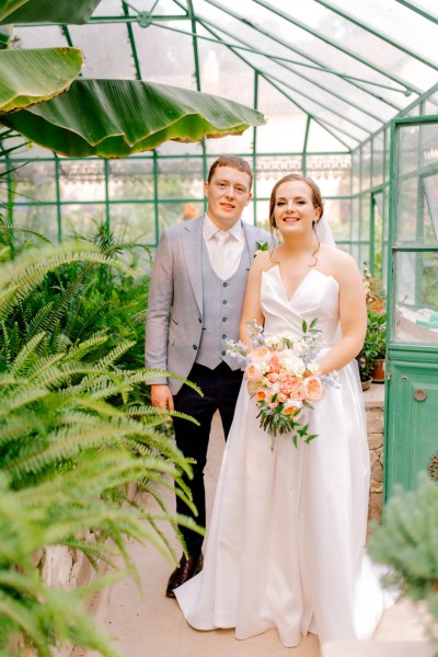 bride and groom in garden she holds bouquet in greenhouse