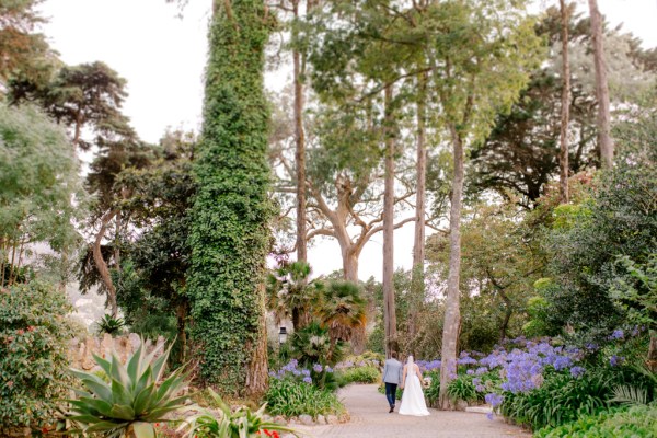 bride and groom in garden she holds bouquet they walk away from camera