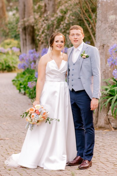 bride and groom walking in forest garden setting on pathway arm around brides waist