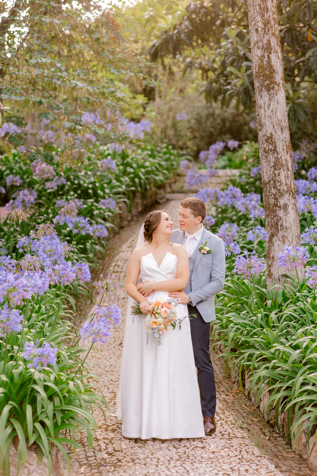 bride and groom walking in forest garden setting on pathway arm around brides waist they face each other