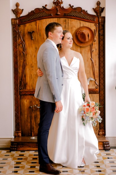 bride and groom stand in room together arms around each other