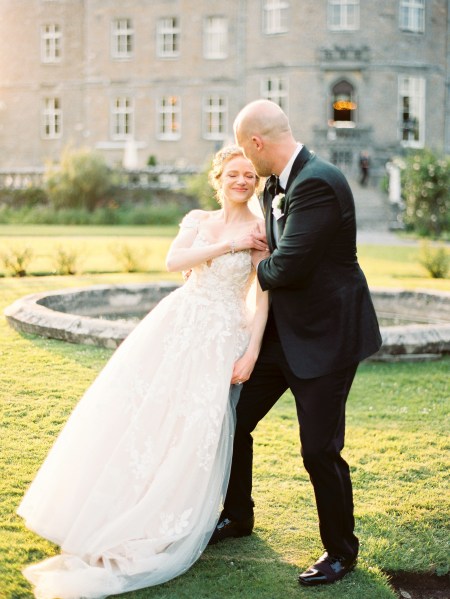 bride and groom dance in front of fountain holding hands castle venue both standing on green grass