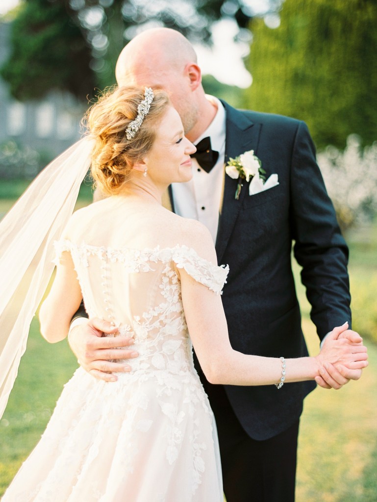 bride and groom dance in front of fountain holding hands castle venue both standing on green grass kiss on the cheek