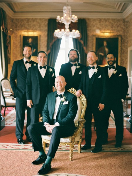 groom and groomsmen sit and stand in Victorian bedroom/room setting