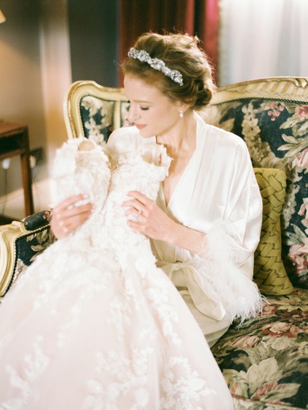 bride holds up bridal gown dress as she stands looking down