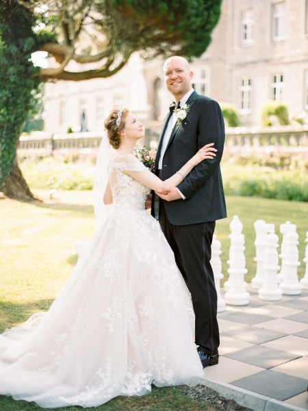 bride and groom stand in garden to wedding venue smiling